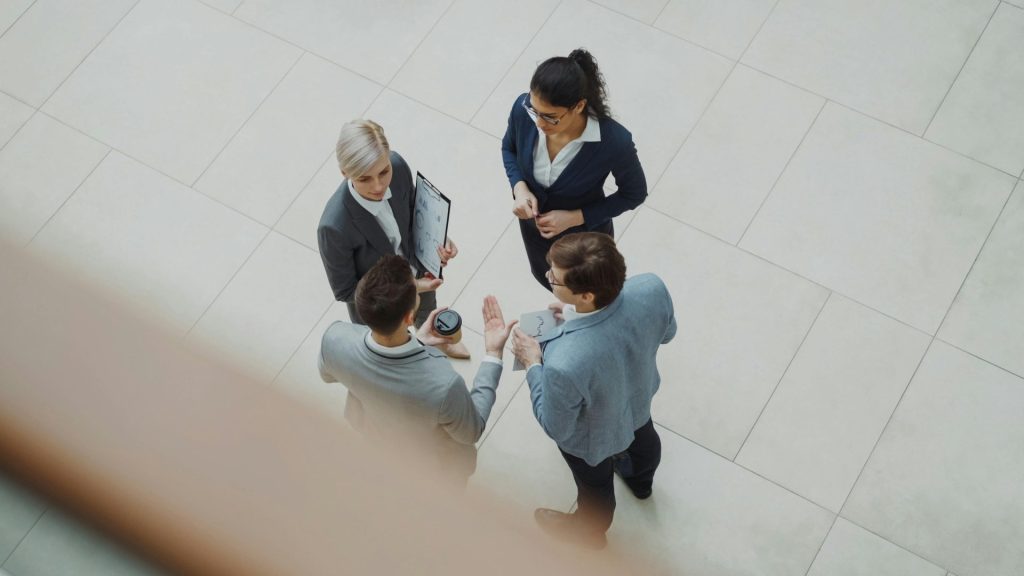 Draufsicht auf ein diverses Business-Team, das in einem Innenraum ein Projekt bespricht.