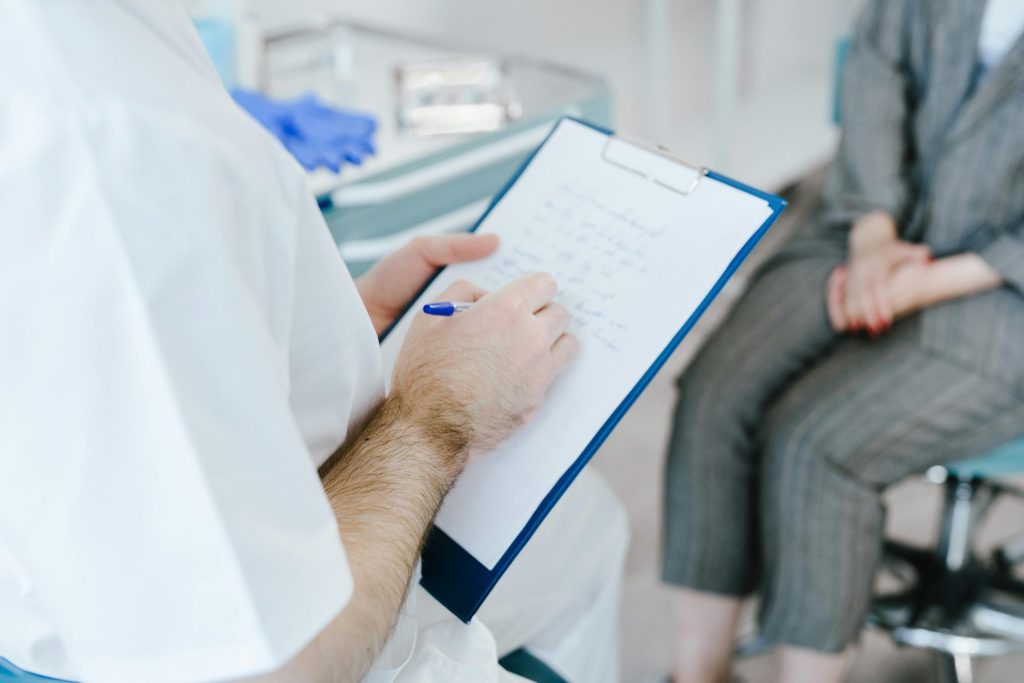 Medizinische Fachkraft fertigt während der Sprechstunde Patientennotizen auf einem Klemmbrett an.