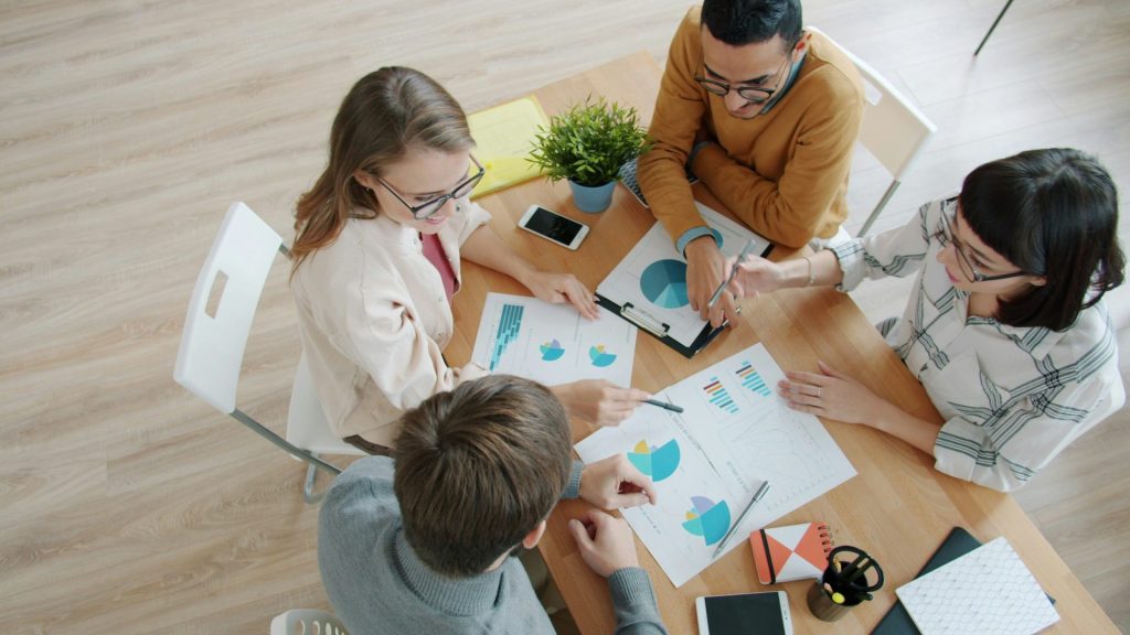 Vier Personen arbeiten gemeinsam an einem Tisch mit Diagrammen.